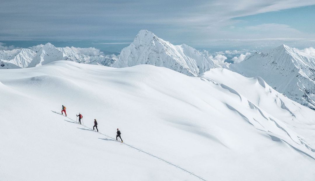 A photo of skiiers racing down snowy mountain peaks in the Alps - Maloja Clothing